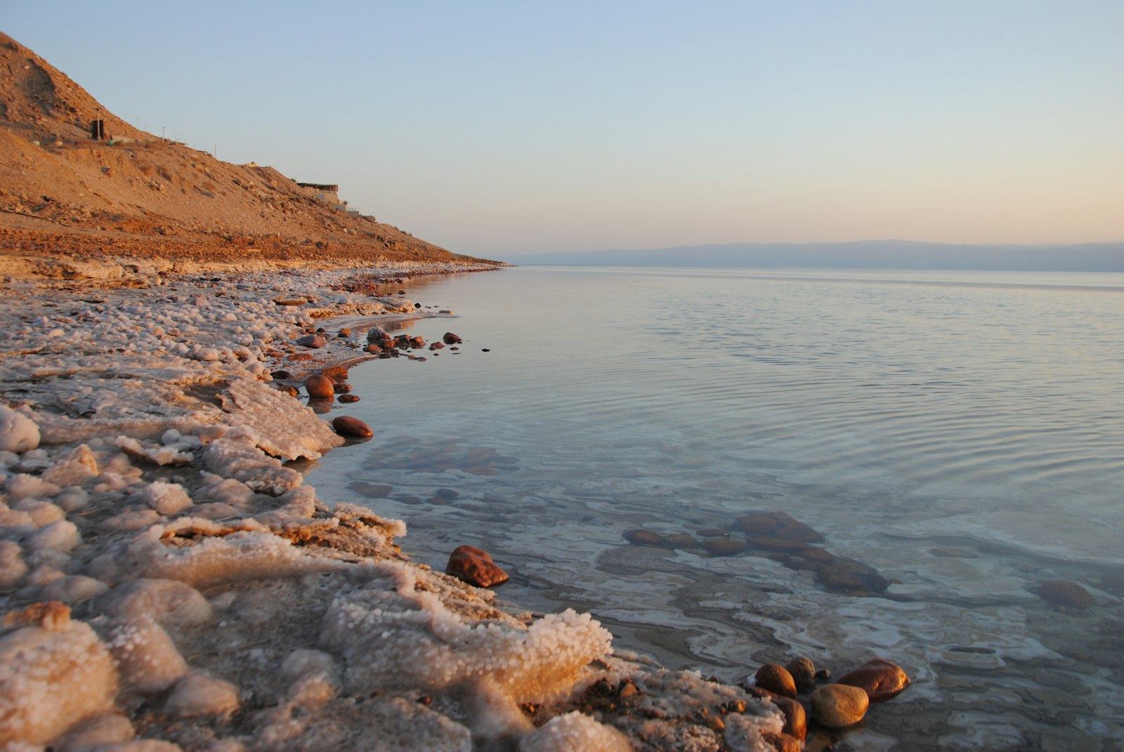 Salt-crusted shoreline of the Dead Sea with still water at low light